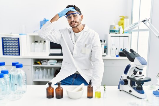 Young hispanic man working at scientist laboratory stressed and frustrated with hand on head, surprised and angry face