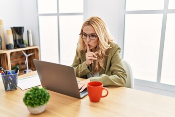 Beautiful blonde woman working at the office with laptop asking to be quiet with finger on lips....
