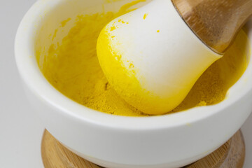 In a mortar, yellow spices are ground with a pestle. Grinding turmeric with a mortar.