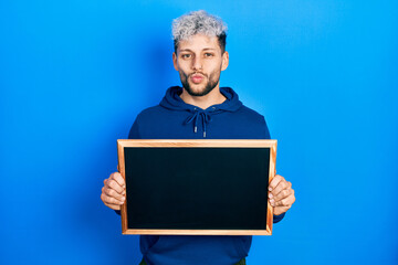 Young hispanic man with modern dyed hair holding blackboard looking at the camera blowing a kiss being lovely and sexy. love expression.