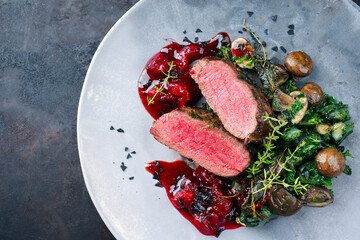 Modern style traditional fried dry aged angus beef filet medaillons natural with mushrooms, kalette and cranberry relish served as top view on a design plate with copy space left