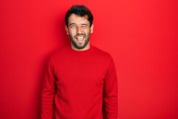Handsome man with beard wearing casual red sweater winking looking at the camera with sexy...
