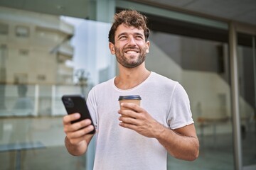 Young hispanic man using smartphone drinking coffee at street