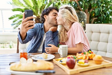 Young couple having breakfast and making selfie by the smartphone smartphone sitting on the table at terrace.