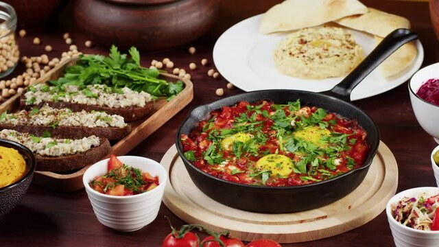 Traditional Israeli cuisine. Putting forshmak on table. Shakshuka in pan decorated with parsley, hummus close-up. National Jewish dishes. Eggs fried in tomato sauce. Middle eastern culture. 