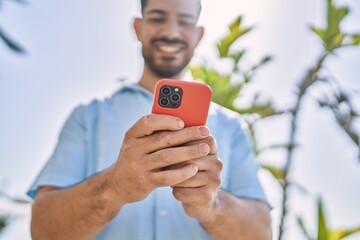 Young hispanic man smiling happy using smartphone at the city.