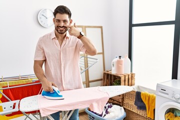 Young man with beard ironing clothes at home pointing with hand finger to face and nose, smiling cheerful. beauty concept