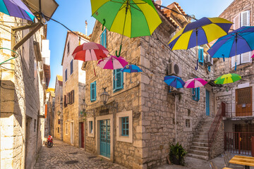 Colorful umbrellas hanging in a stone street in the historic center of Trogir town, Croatia, Europe.