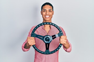 Young african american guy holding steering wheel smiling with a happy and cool smile on face. showing teeth.