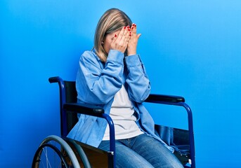 Beautiful caucasian woman sitting on wheelchair with sad expression covering face with hands while crying. depression concept.