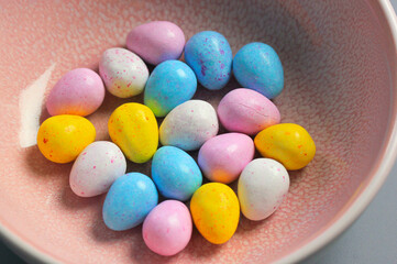 Multicolored chocolate Easter eggs yellow pink blue colors are lying in pastel pink bowl top view. Sweets, treats for children, kids in spring season holiday. Festive junk food in plate. Easter bunny.