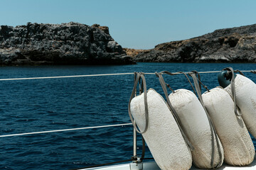 Fenders up in row on board of sailing boat, rocky coat and sea or ocean on background
