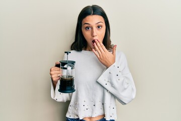 Young hispanic woman drinking italian coffee covering mouth with hand, shocked and afraid for mistake. surprised expression