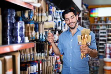 Smiling man choosing tools for home renovation in paint store