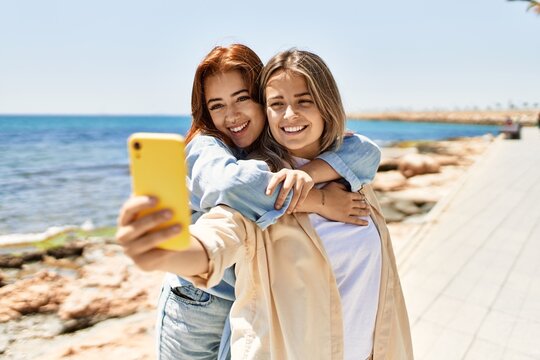 Young lesbian couple of two women in love at the beach. Beautiful women together at the beach in a romantic relationship taking selfie photo with smartphone