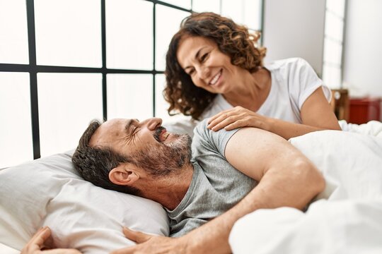 Middle age hispanic woman waking up her husband lying on the bed at home.