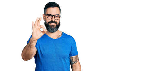 Hispanic man with beard wearing casual t shirt and glasses smiling positive doing ok sign with hand and fingers. successful expression.