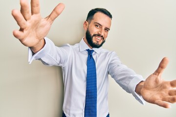 Young man with beard wearing business tie looking at the camera smiling with open arms for hug. cheerful expression embracing happiness.