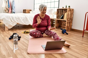 Middle age grey-haired woman training having video call sitting on the floor at bedroom.