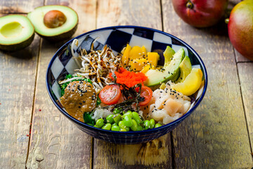 scallop poke with mango, avocado, tomatoes, chukka, edamame and boiled rice on blue plate on wooden table