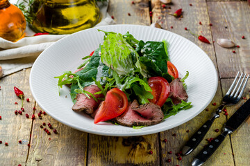Salad with roast beef and vegetables on white plate on wooden table