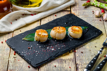 grilled scallop on black stone on wooden table
