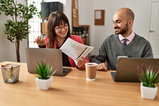 Two hispanic business workers smiling happy working using laptop and smartphone at the office.