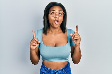 Young african american girl wearing casual clothes amazed and surprised looking up and pointing...