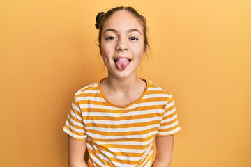 Beautiful brunette little girl wearing casual striped t shirt sticking tongue out happy with funny...