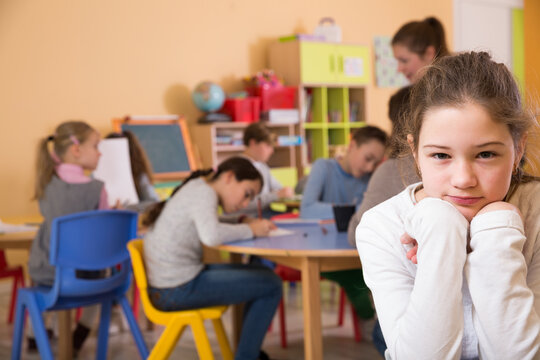 Portrait of sad unhappy schoolgirl and children drawing in classroom