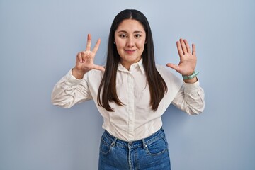 Young latin woman standing over blue background showing and pointing up with fingers number eight while smiling confident and happy.