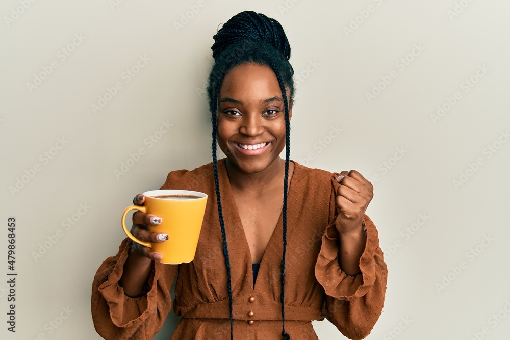 Poster African american woman with braided hair drinking a cup coffee screaming proud, celebrating victory and success very excited with raised arm