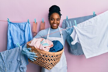 African american woman with braided hair doing laundry holding wicker basket doing ok sign with...