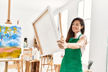 Fototapeta na wymiar Middle age hispanic woman smiling confident holding canvas draw at art studio