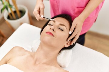 Middle age hispanic woman having eyebrows treatment at beauty center