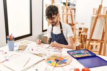 Young hispanic artist man smiling happy drawing at art studio.
