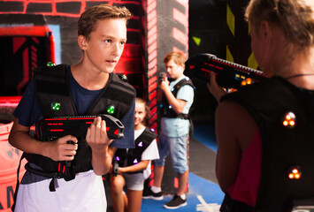 Fototapeta na wymiar Emotional teen boy with laser pistol playing laser tag with friends on dark labyrinth..