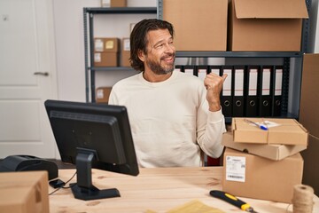 Handsome middle age man working at small business ecommerce smiling with happy face looking and pointing to the side with thumb up.