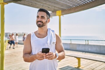 Hispanic sports man wearing workout style using smartphone outdoors on a sunny day