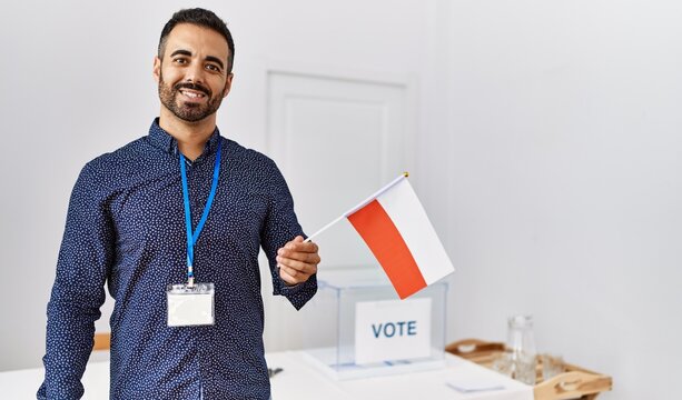 Young hispanic man smiling confident holding poland flag standing at electoral college