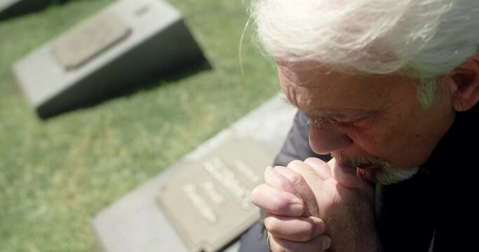 Sad old gray haired man prays on the grave at the cemetery. Sorrow and sadness. Religiuos man, 4k 60p Prores