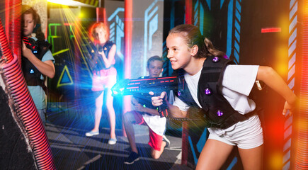 Fototapeta na wymiar Portrait of teenager girl with laser gun having fun on dark lasertag arena..