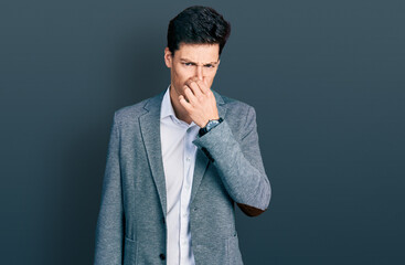 Young hispanic man wearing business clothes smelling something stinky and disgusting, intolerable...