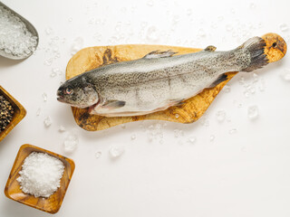Raw fresh fish on a wooden cutting board, near in wooden bowls salt and spices. White background. High angle view. Preparation of fish dishes. Restaurant, hotel, cafe, culinary blog, instagram.