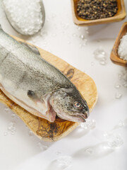 Fresh fish carcass on a cutting wooden board. In the background there are wooden bowls with salt and spices. White background. Macro photography. Advertising, fish market, fish and seafood dishes.