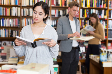 Intelligent adult girl browsing textbooks in bookstore