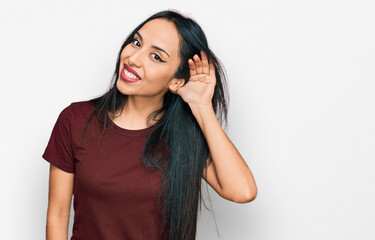 Fototapeta premium Young hispanic girl wearing casual t shirt smiling with hand over ear listening an hearing to rumor or gossip. deafness concept.