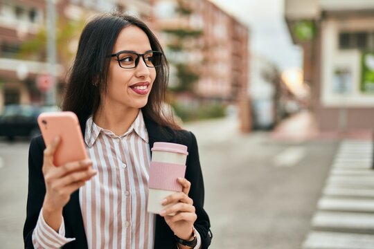 Young hispanic businesswoman using smartphone drinking coffee at the city.