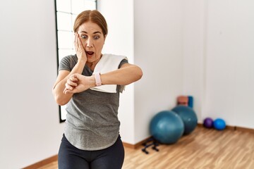 Fototapeta na wymiar Middle age woman wearing sporty look training at the gym room looking at the watch time worried, afraid of getting late