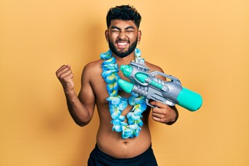 Arab man with beard wearing swimsuit and hawaiian lei holding watergun screaming proud, celebrating...